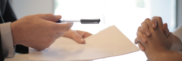 Un personne tend un papier et un stylo à une autre, représentant un gestionnaire immobilier qui fait signer un mandat de gestion locative à un bailleur.