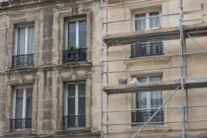 Ravalement de façade d’un immeuble en pierre de taille : partie encrassée à gauche, partie nettoyée sous échafaudage à droite