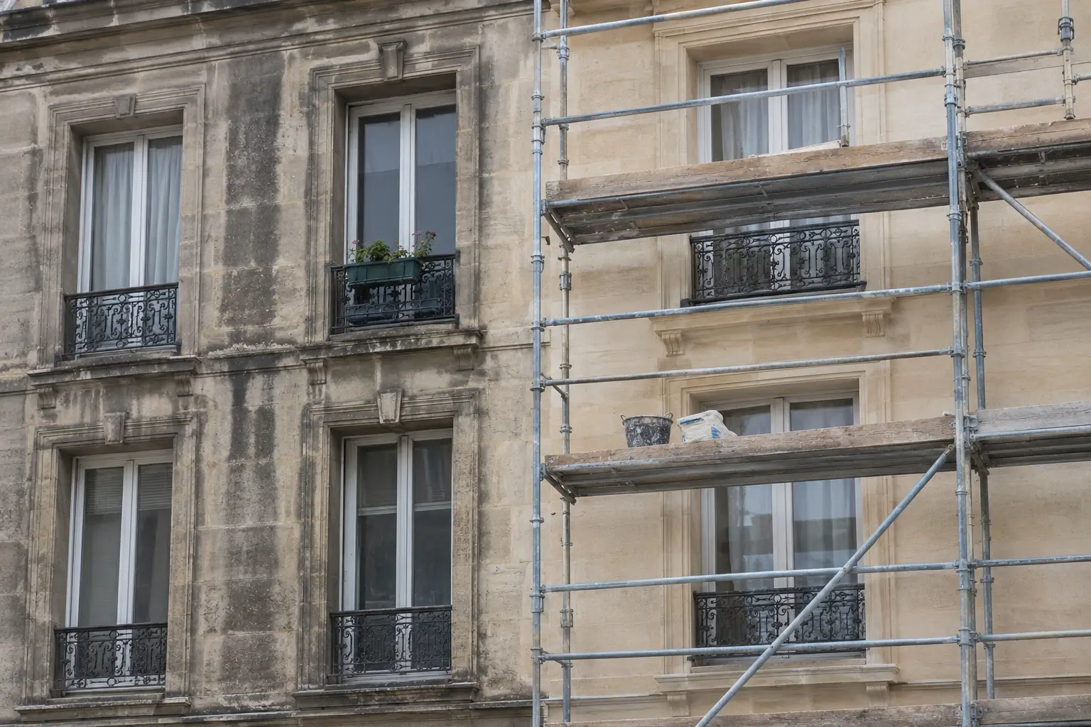 Ravalement de façade d’un immeuble en pierre de taille : partie encrassée à gauche, partie nettoyée sous échafaudage à droite